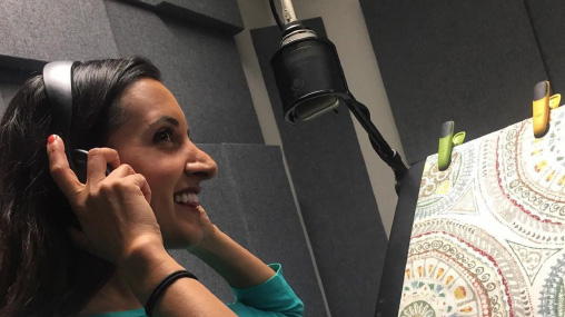 Paula Pant recording the Afford Anything podcast in a studio, wearing headphones while speaking into a professional microphone, embodying her mission to teach listeners about financial independence.